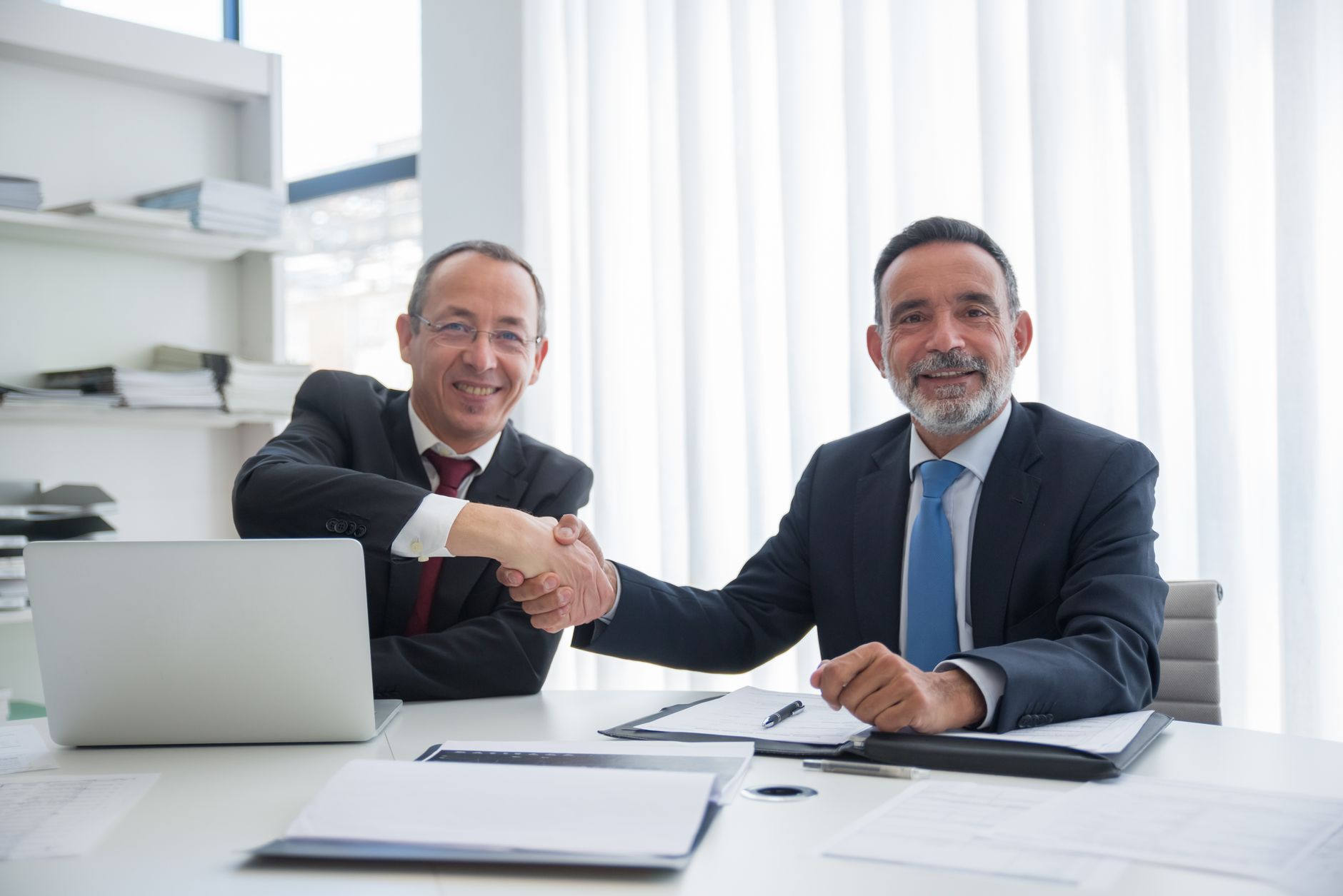 Two businessmen shaking hands across a table in an office