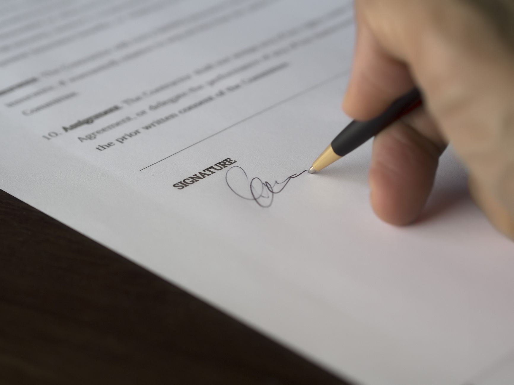A hand signing a formal contract with a pen on a desk