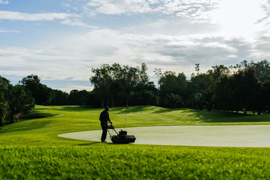 Groundskeeper mowing a lush green lawn on a sunny day