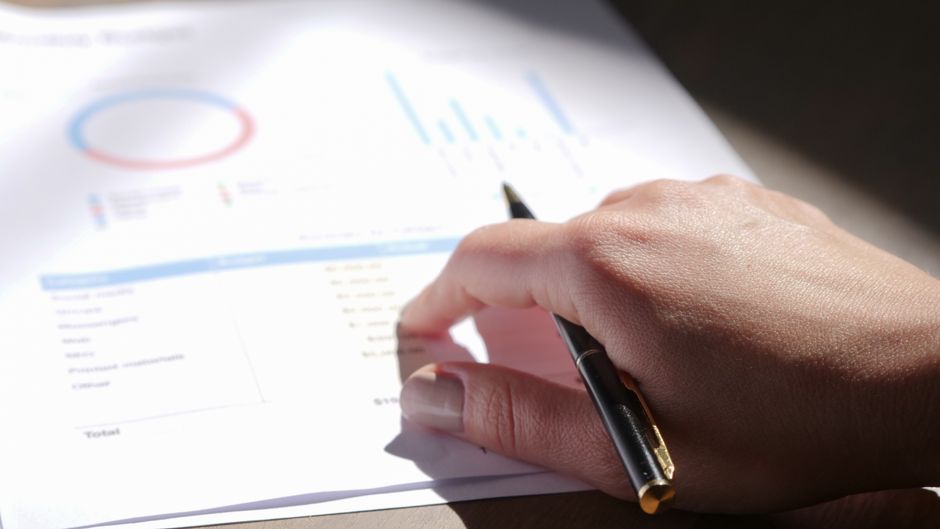 A hand reviewing financial documents with a pen